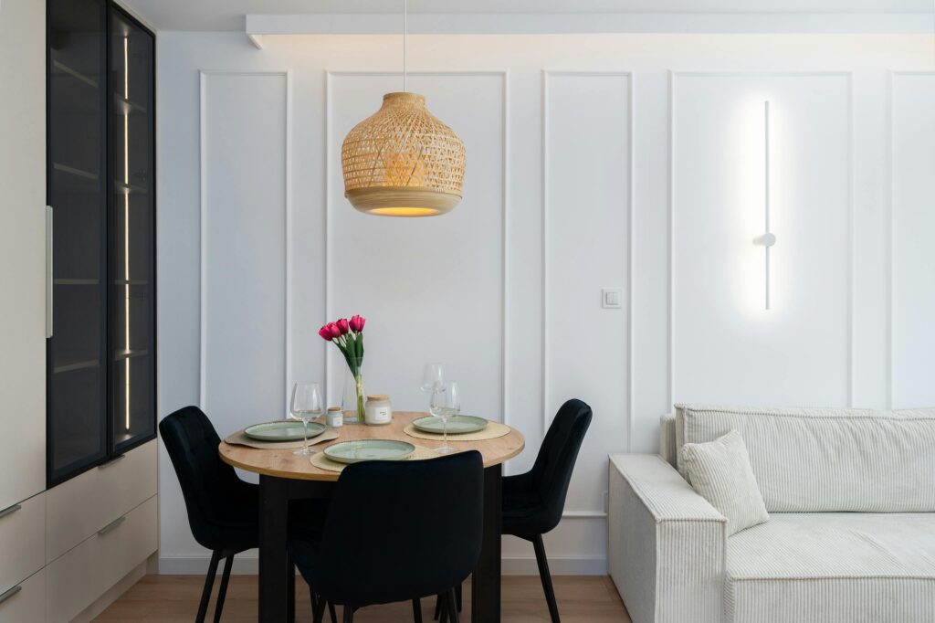 pexels-mateusz-pielech-1032276948-33054907 Modern dining room with round table, black chairs, pendant light, and pink tulips centerpiece. Cozy white sofa adjacent. | Sky Rye Design Modern dining room with round table, black chairs, pendant light, and pink tulips centerpiece. Cozy white sofa adjacent.