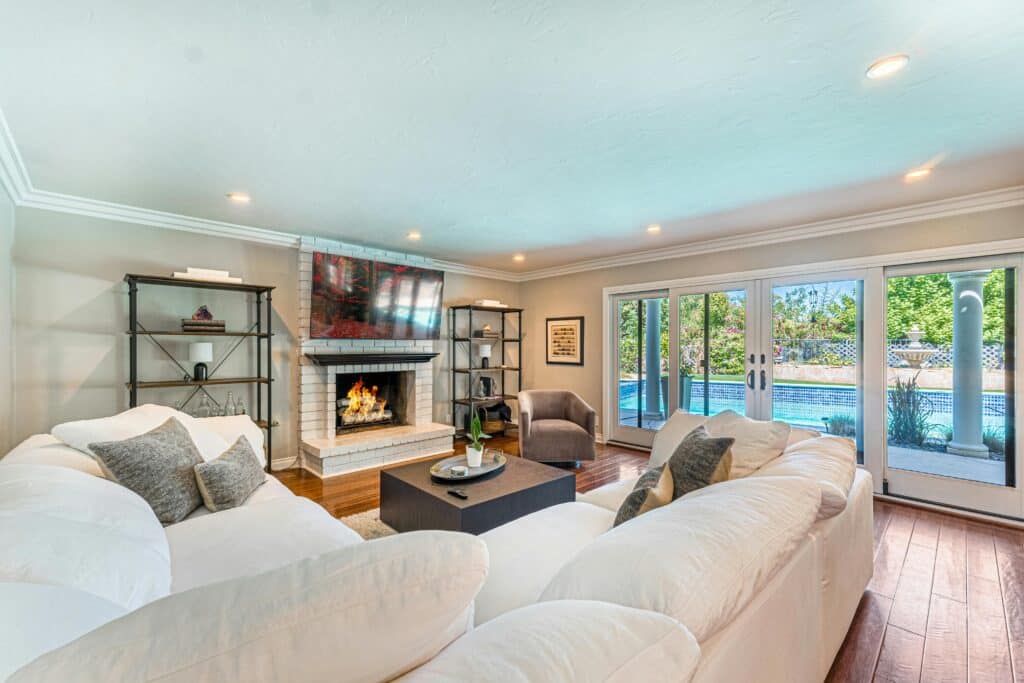 pexels-photo-28272352 Cozy living room with fireplace, large windows, pool view, and plush seating. | Sky Rye Design Cozy living room with fireplace, large windows, pool view, and plush seating.