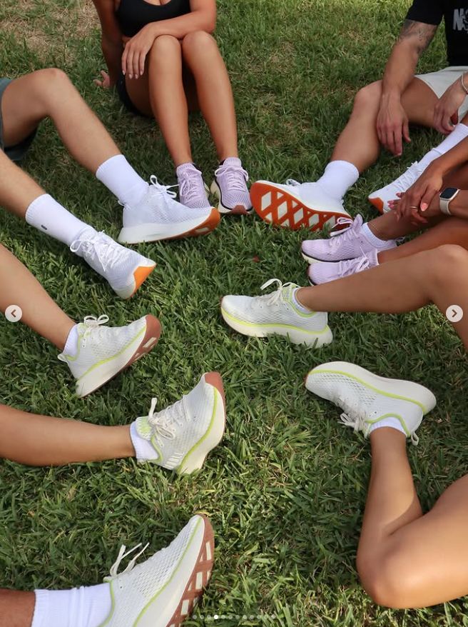 Group of people sitting on grass, showcasing stylish sneakers with colorful soles. Perfect for outdoor activities.