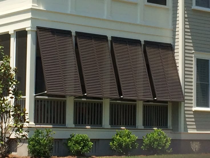 Brown exterior window shutters providing shade on a light-colored house.