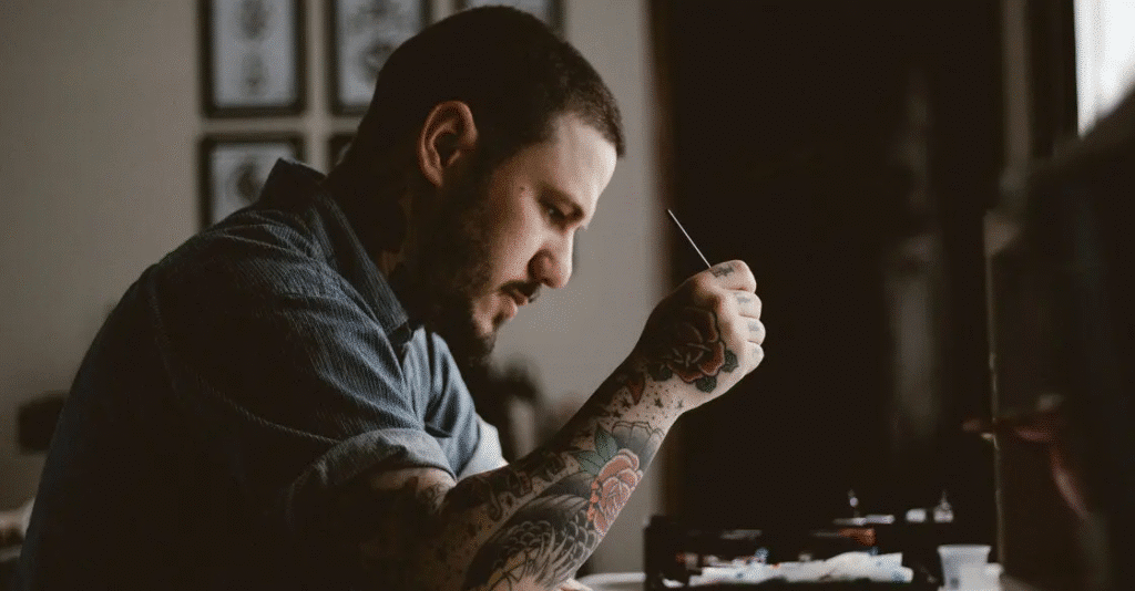 Tattooed artist focused on painting in a dimly lit studio, showcasing creativity and dedication to art.