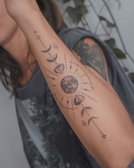 Arm tattoo of lunar phases and sun with detailed line work on a person's forearm, set against a leafy background.