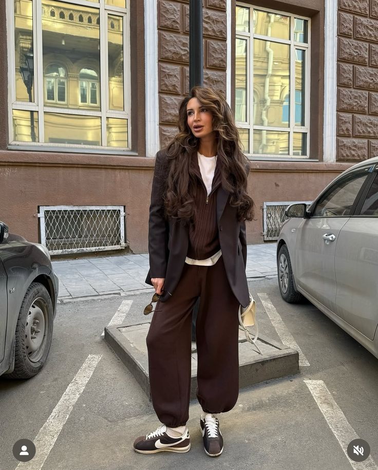 Woman in chic winter outfit with brown blazer and sneakers, standing on city street.