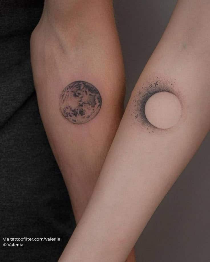 Two forearms with matching sun and moon tattoos, symbolizing balance and connection.