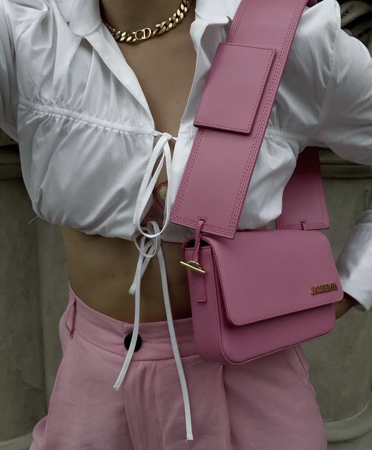 Stylish woman wearing a white crop top with a pink bag and shorts, accessorized with a chunky gold necklace.