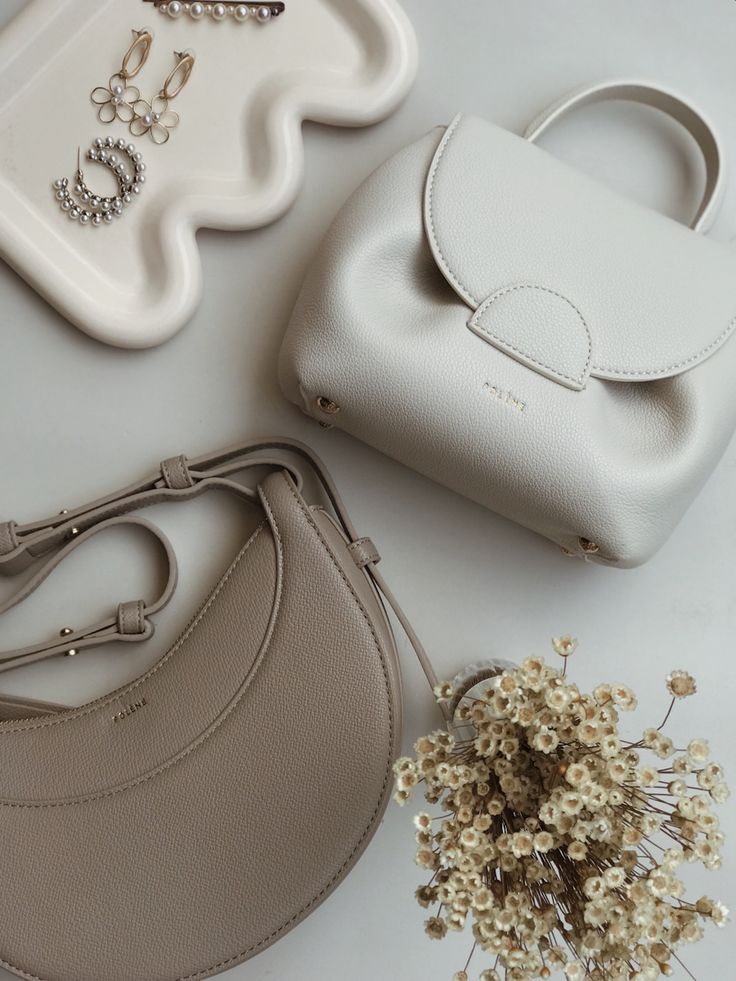 Elegant handbags and jewelry on a tray with dried flowers, showcasing minimalist fashion accessories.