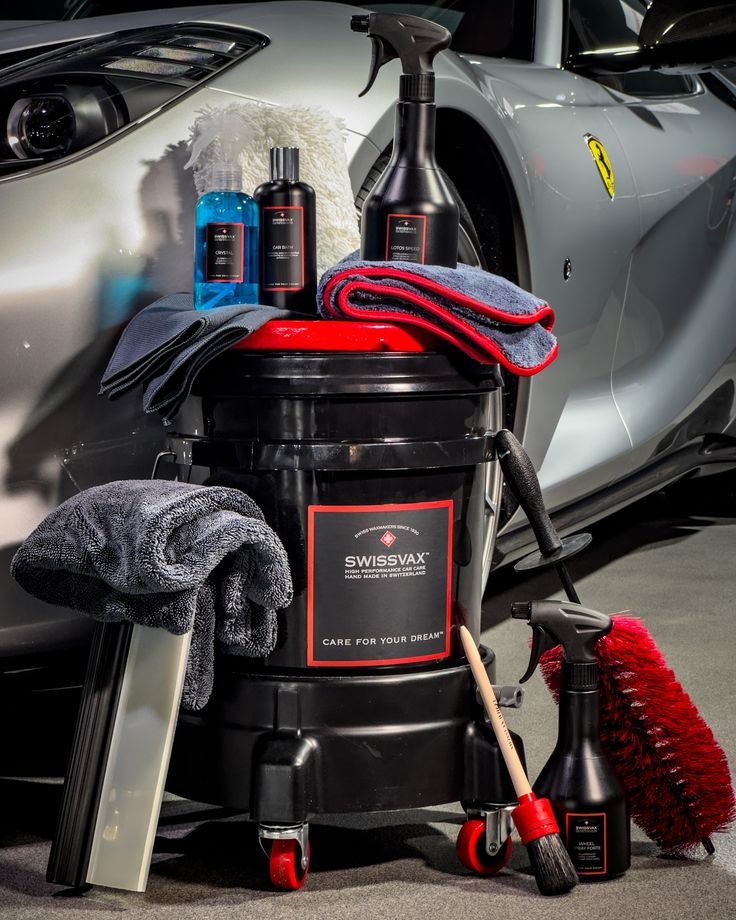 Car detailing products next to a luxury car, featuring Swissvax cleaning supplies and microfiber towels.