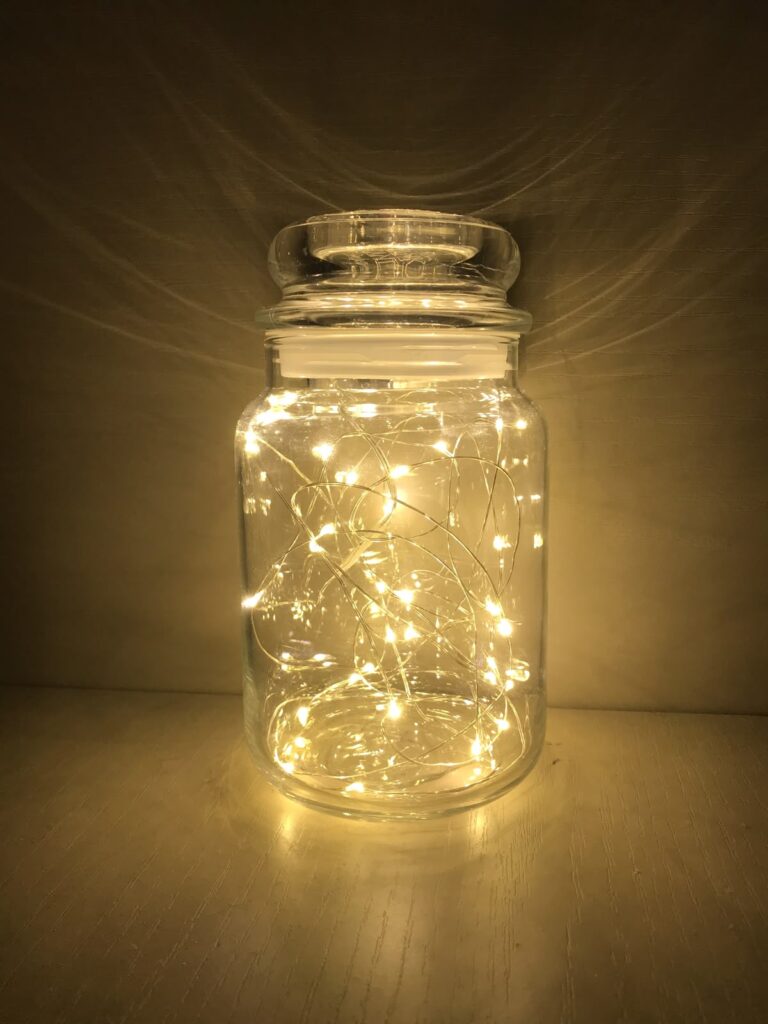 Glowing fairy lights in a glass jar creating a warm, ambient atmosphere in a dimly lit room.