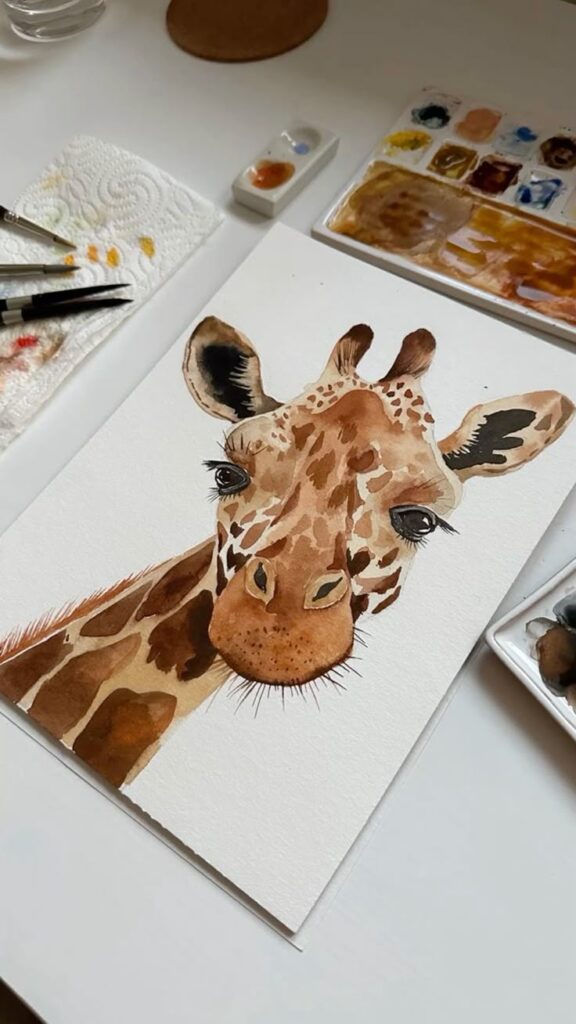 Watercolor painting of a giraffe on a desk with art supplies, showcasing detailed brushwork and vibrant colors.