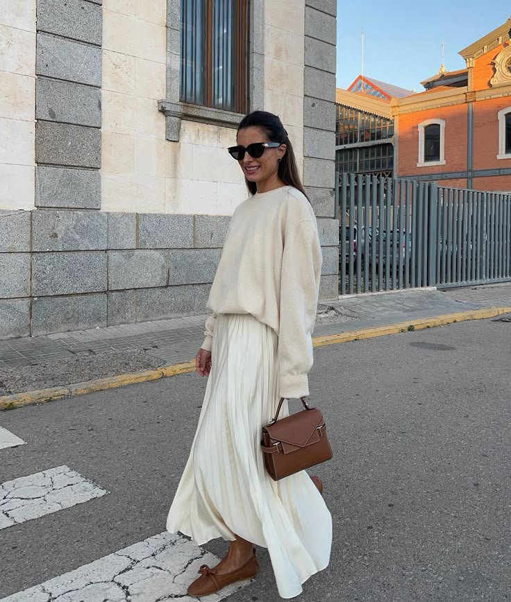 Woman in stylish minimalist outfit with sunglasses and brown purse walks on urban street.