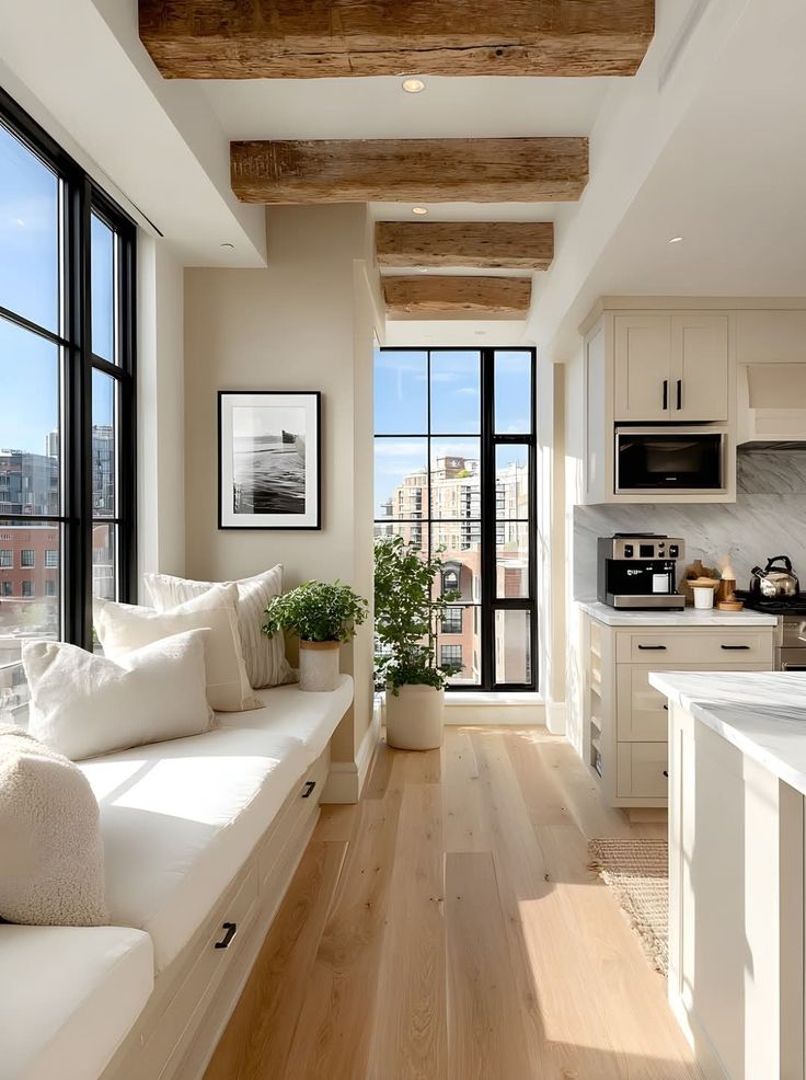 Modern kitchen with exposed wooden beams, cozy seating, plants, and large windows overlooking a cityscape.