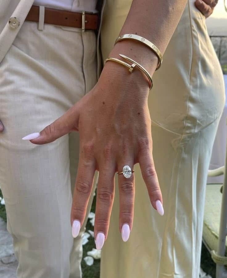 Hand displaying engagement ring and gold bracelets against cream outfits, highlighting elegant jewelry and fashion.