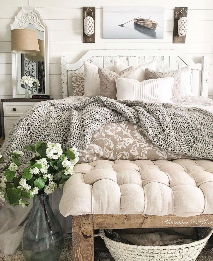 Cozy farmhouse bedroom with tufted bench, knit throw, and floral vase for stylish rustic decor.