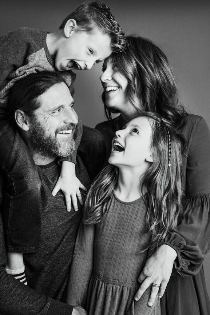 A joyful family smiling and enjoying a playful moment together in a black and white portrait.