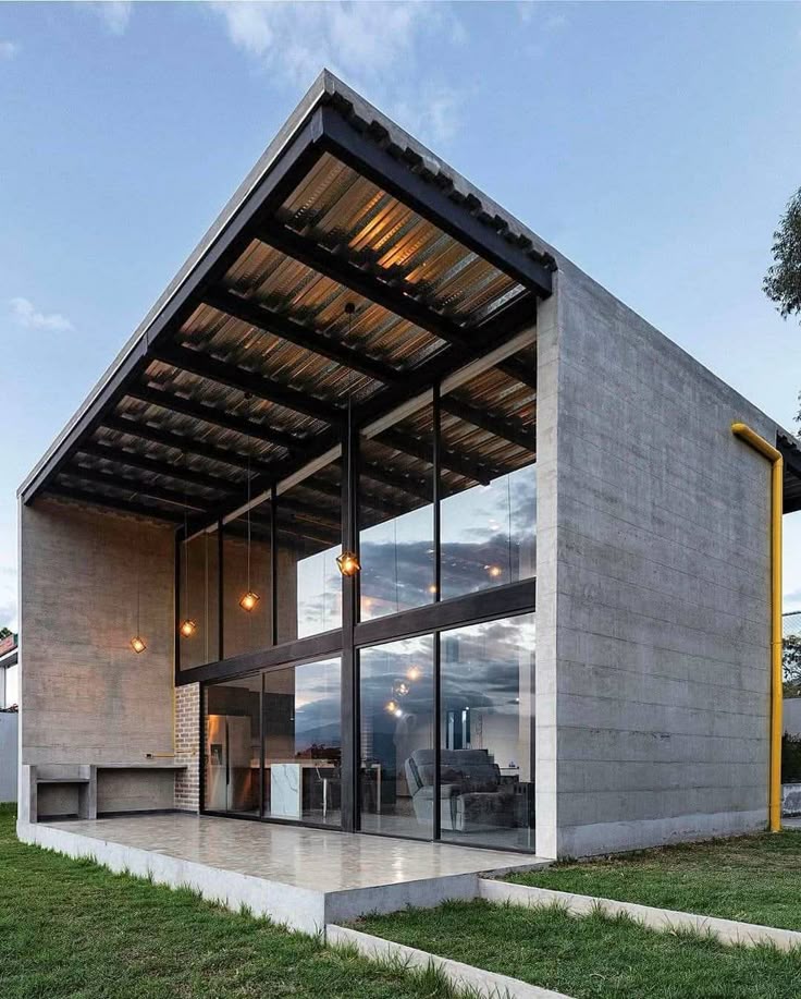 Modern concrete house with large glass windows and sloped roof at sunset.
