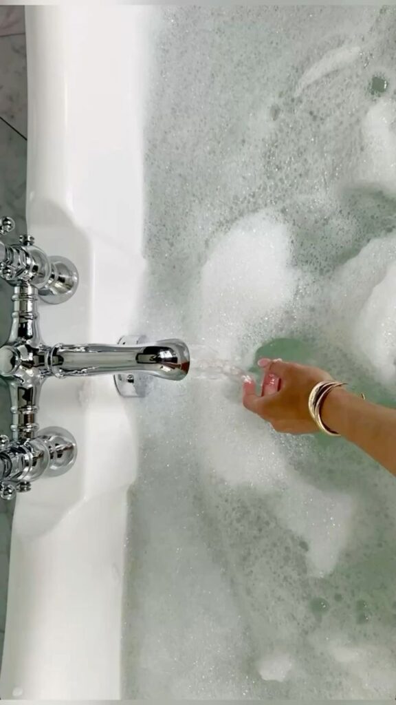 Hand testing warm water in a luxurious bubble bath, silver faucet flowing smoothly.
