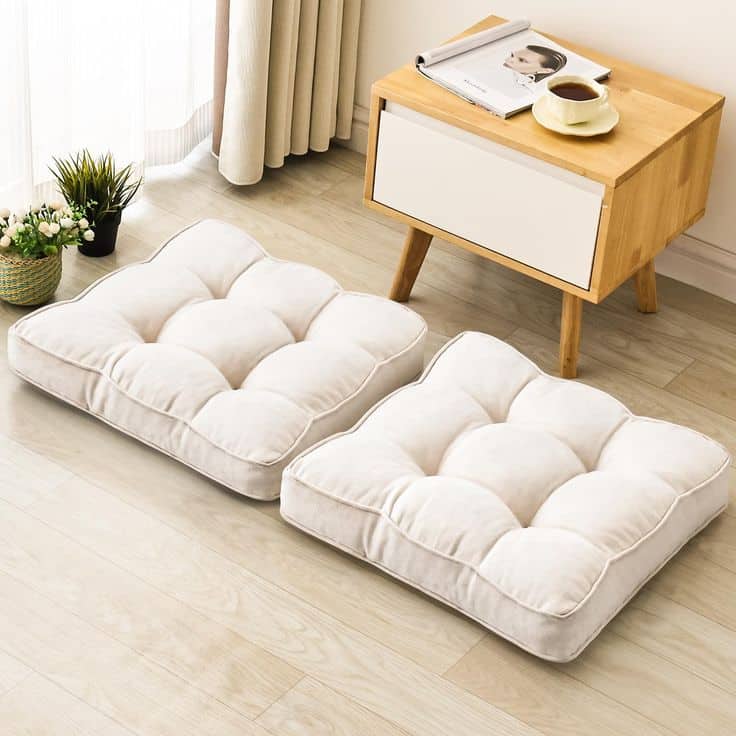 Two plush floor cushions next to a small wooden table with a cup and magazine, cozy room setup.
