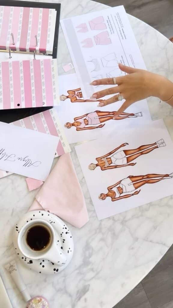 Fashion design sketches on marble table with color swatches, coffee cup, and fabric samples.