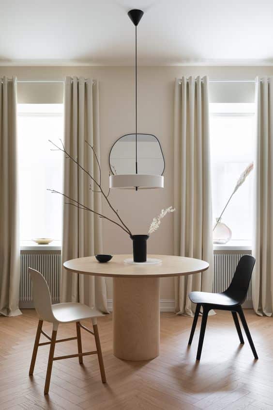 Minimalist dining room with round table, two chairs, pendant light, and neutral decor.