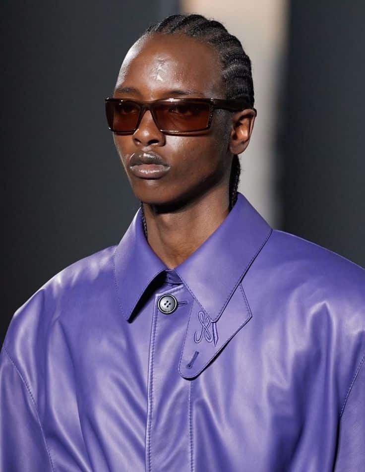 Model in purple leather jacket and sunglasses on fashion runway.
