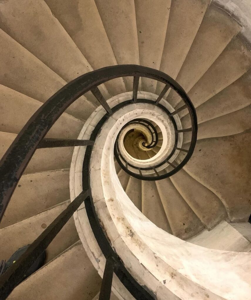 Spiral staircase with a metal railing, viewed from above, creating a mesmerizing geometric pattern.