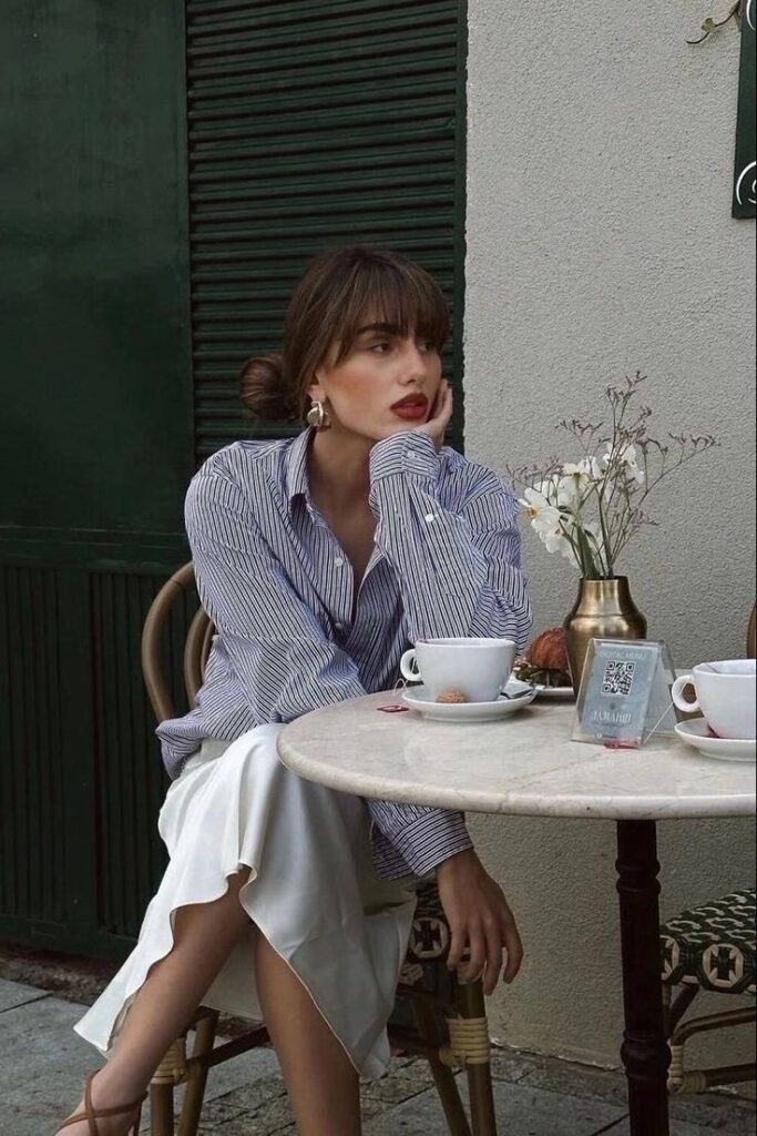 Woman in striped blouse seated at outdoor café, looking pensive with coffee on marble table.