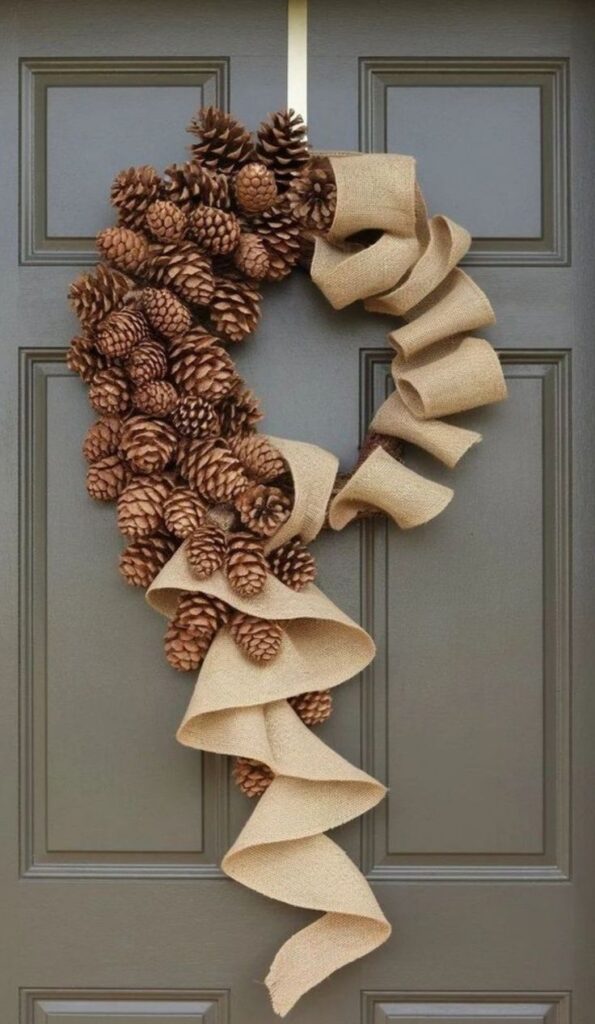 Pinecone and burlap ribbon wreath on a dark door, perfect for seasonal or rustic decor enthusiasts.