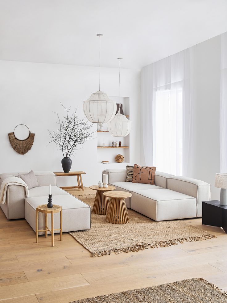 Minimalist living room with neutral sofas, natural wood tables, pendant lights, and woven decor accents.