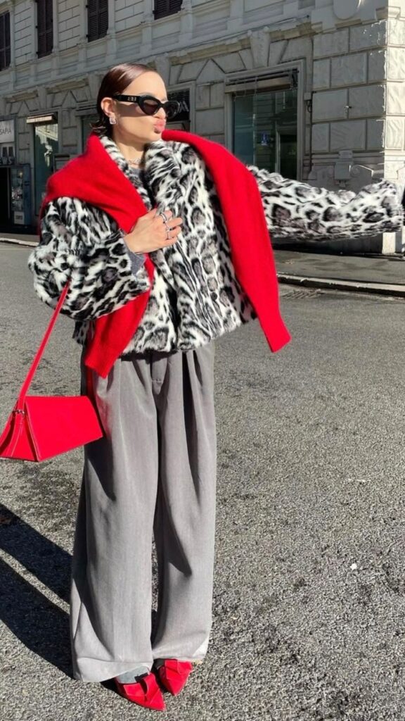 Fashion-forward woman in stylish leopard print coat, red scarf, and sunglasses, striking a pose on an urban street.