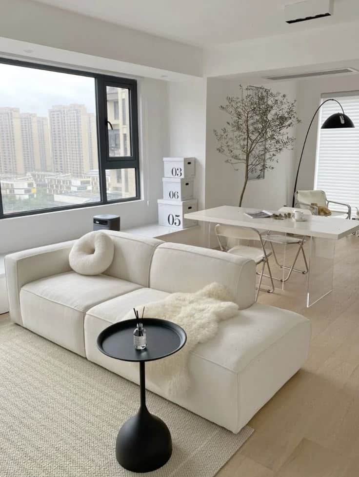 Modern minimalist living room with white sofa, black table, and large window view of cityscape.