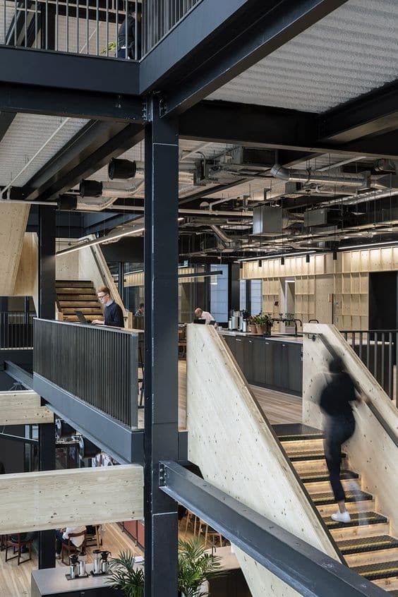 Modern office interior with open stairways, industrial design, and people working, showcasing contemporary workspace architecture.