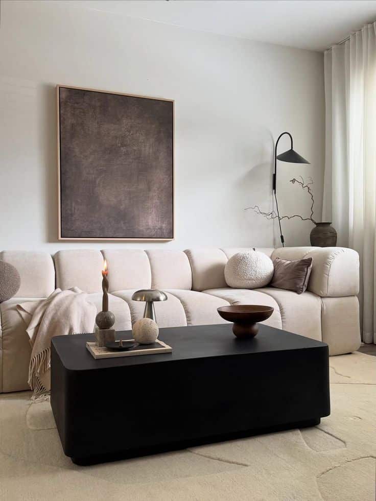 Modern living room with beige sofa, black coffee table, and minimalist decor, featuring a large abstract wall art.