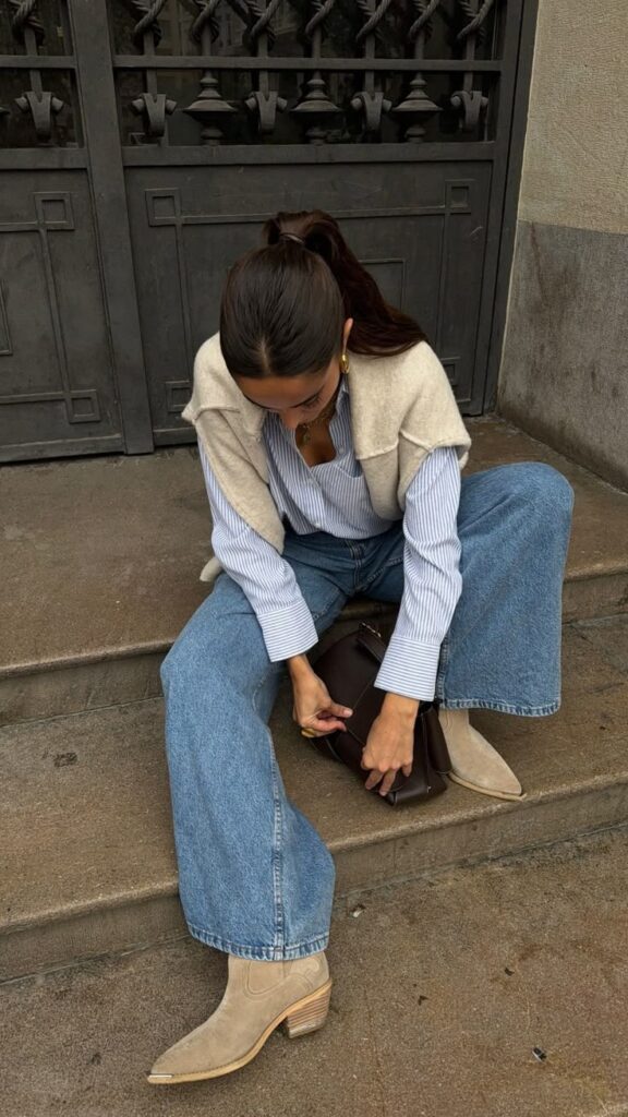 Woman in casual jeans and boots ties a bag on concrete steps, showcasing chic street style.