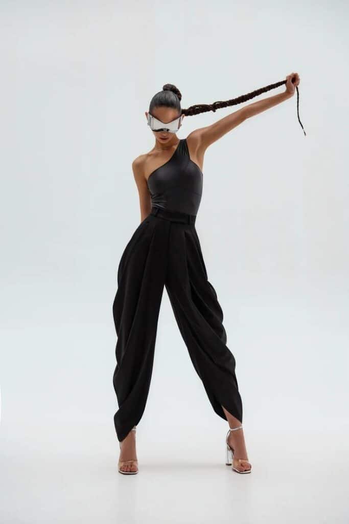Fashion-forward model in black outfit and futuristic sunglasses, striking a pose on a minimalist white background.