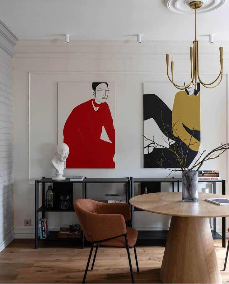 Modern living room with abstract art, wooden table, orange chair, black shelving, and a decorative chandelier.
