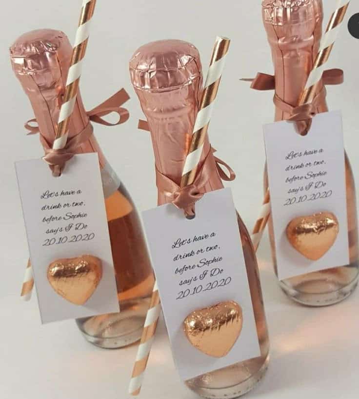 Mini champagne bottles with tags, straws, and heart chocolates, perfect for pre-wedding celebration.