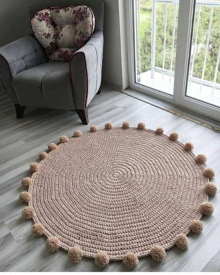 Cozy living room with a round, woven rug and an armchair by a sunny window.