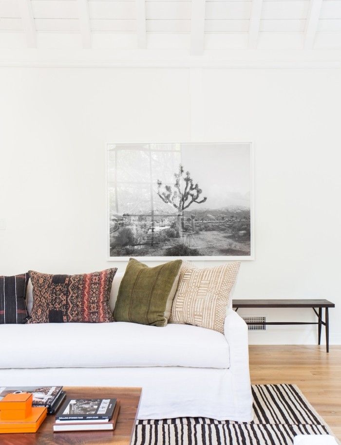 Modern living room with white sofa, decorative pillows, nature artwork, and wooden floor for a cozy minimalist design.