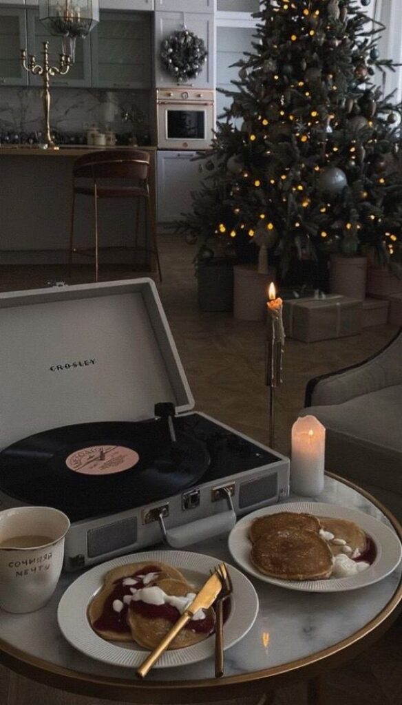 Cozy holiday scene with pancakes, candlelight, a record player, and a decorated Christmas tree in the background.