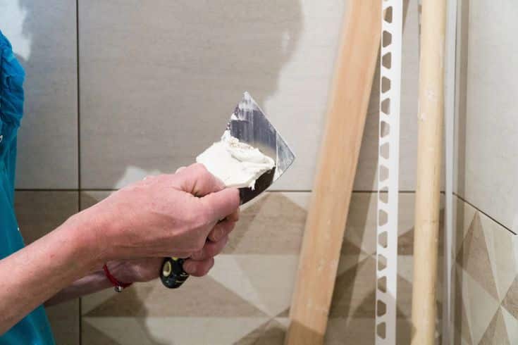 Person applying grout to bathroom tiles using a trowel during a renovation project.