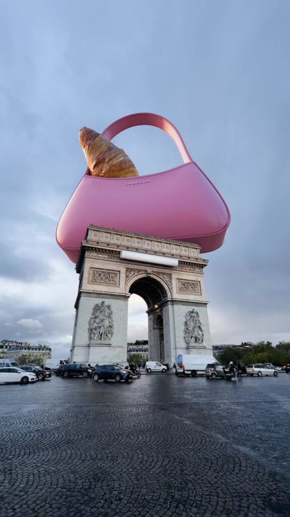 Surreal image of Arc de Triomphe with a giant pink handbag and croissant on top, blending fashion with iconic Paris monument.