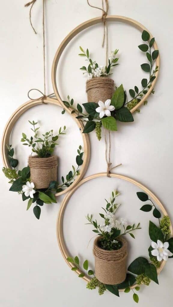 Hanging hoop decor with white flowers and greenery in jute pots on a white wall.