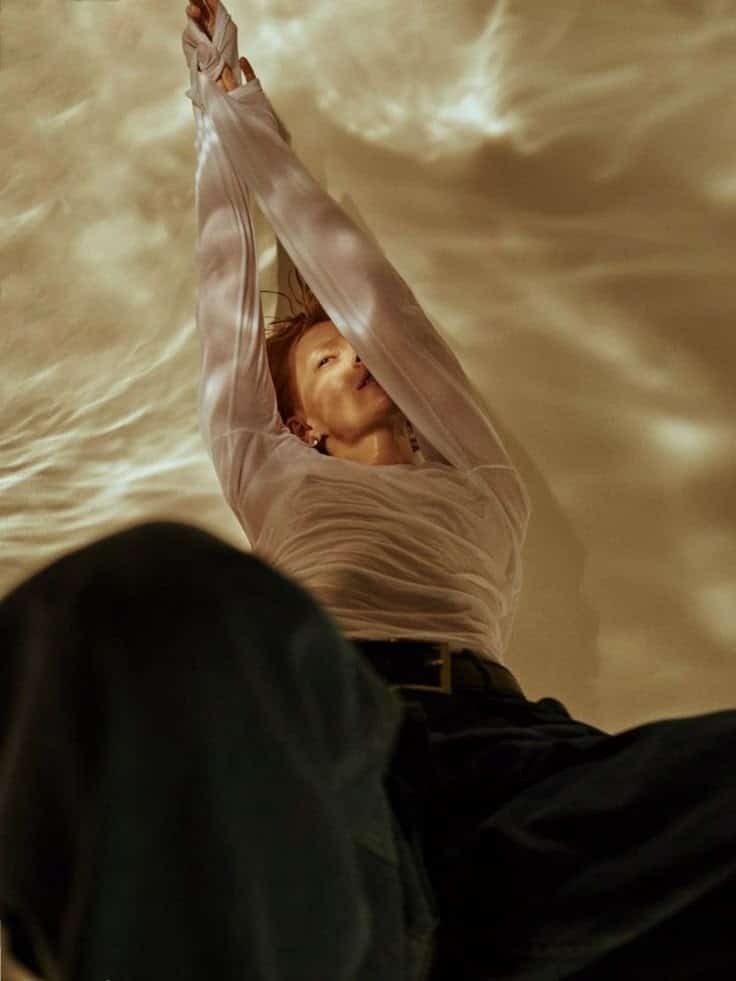 Person in sheer top stretching gracefully under soft, golden lighting.