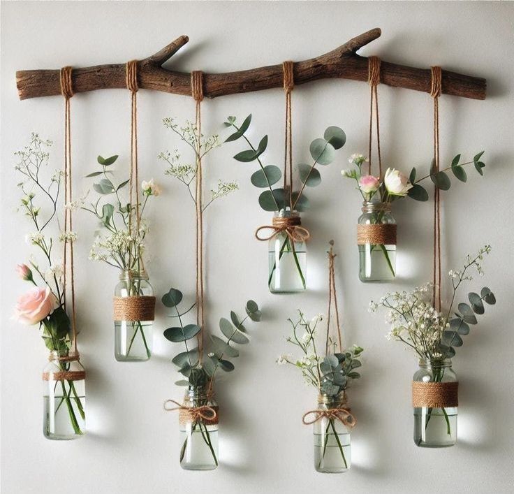 Hanging glass jars with flowers on branch, creative wall decor with roses and greenery in rustic style.