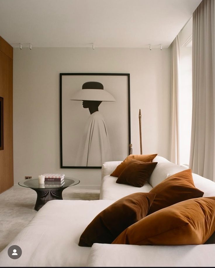 Modern living room with a chic black-and-white portrait, white sofa, and rust-colored pillows.