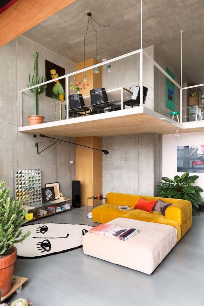Modern loft with vibrant decor, yellow couch, cacti, and a mezzanine dining area in an industrial-style open space.