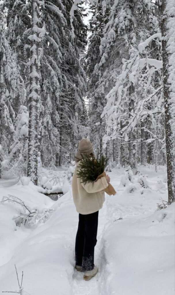 Person holding evergreen branches in a snowy forest, creating a peaceful winter scene.