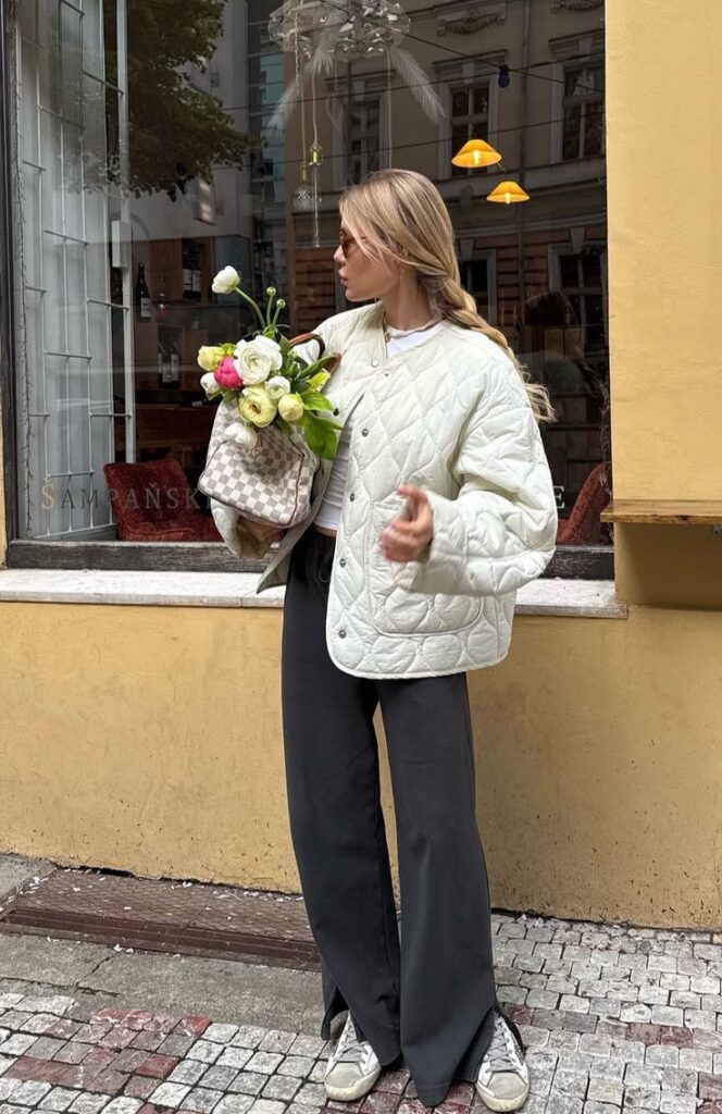 Woman in quilted jacket with bouquet in urban setting. Fashionable street style, casual and chic.