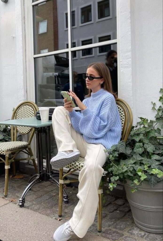 Woman in blue sweater and sunglasses using smartphone at an outdoor cafe.