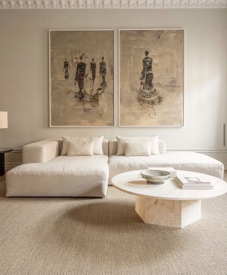 Minimalist living room with large beige sectional, abstract art, and round marble coffee table on textured rug.
